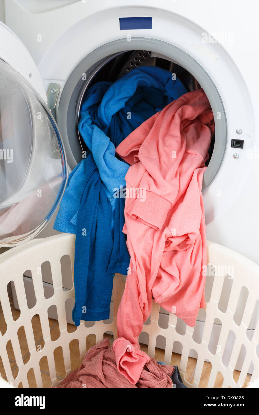 Washed clothes being taken out of open door of a front loading washing machine into a laundry basket Stock Photo