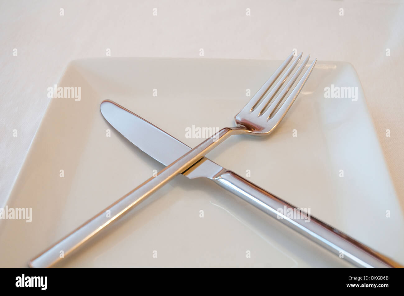 Crossed fork and knife on an empty plate. Close view. Stock Photo