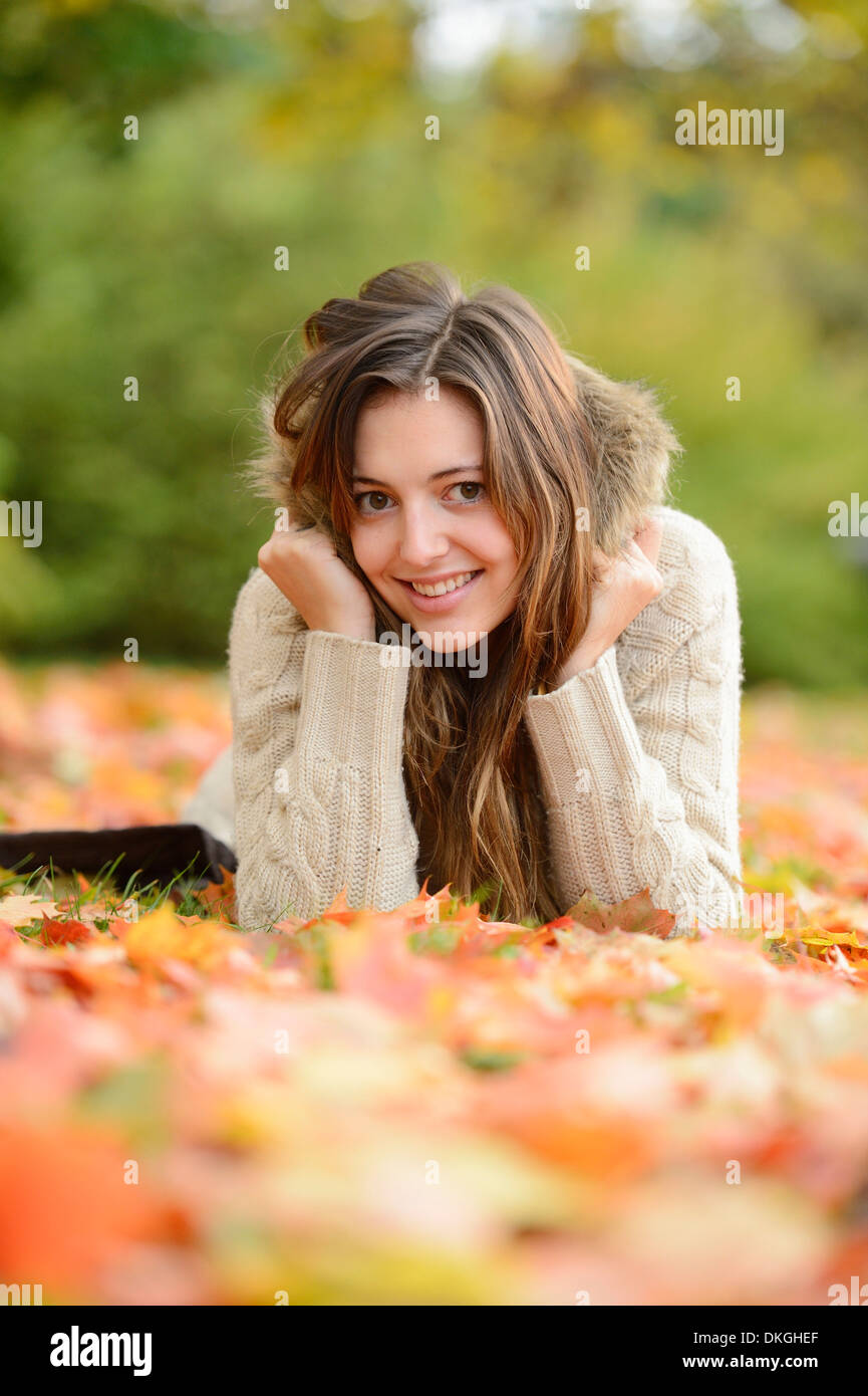 Smiling young woman lying in autumn leaves Stock Photo