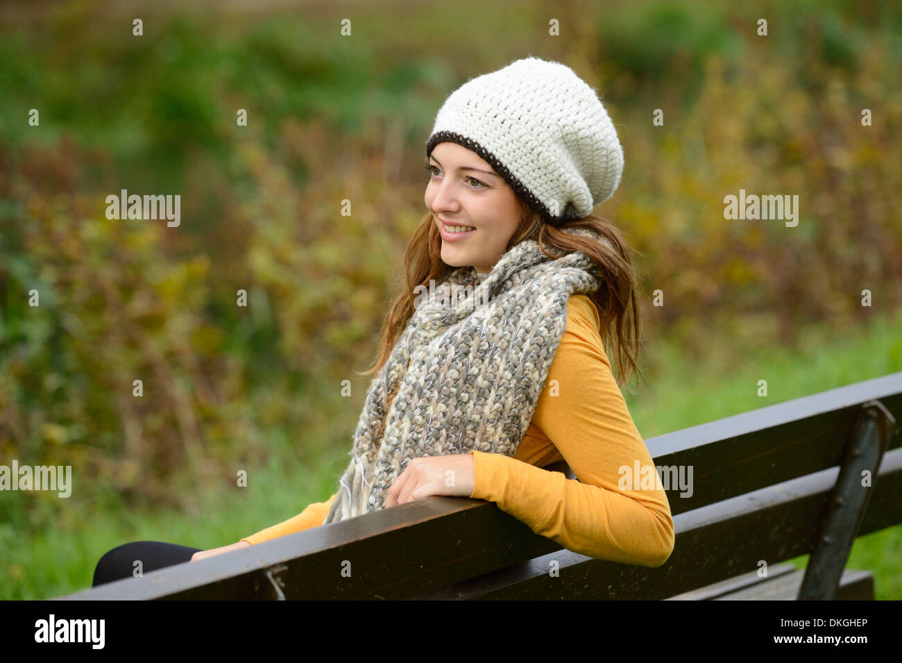 Smiling young woman sitting on a bench in autumn Stock Photo