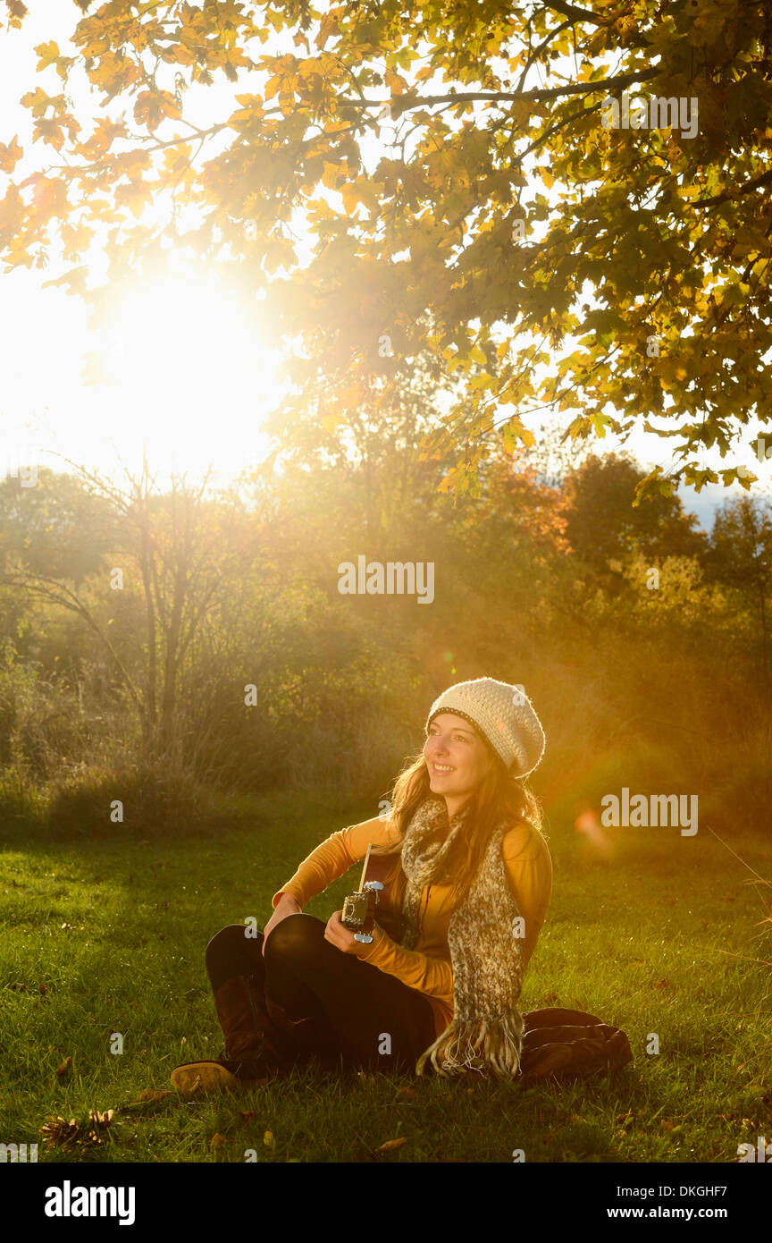 Smiling young woman playing guitar in autumn Stock Photo