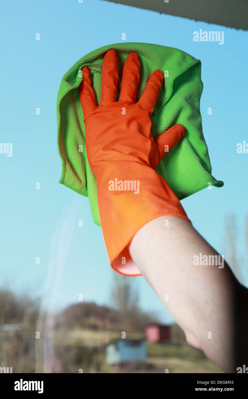 hand in orange glove cleaning window with green rag Stock Photo