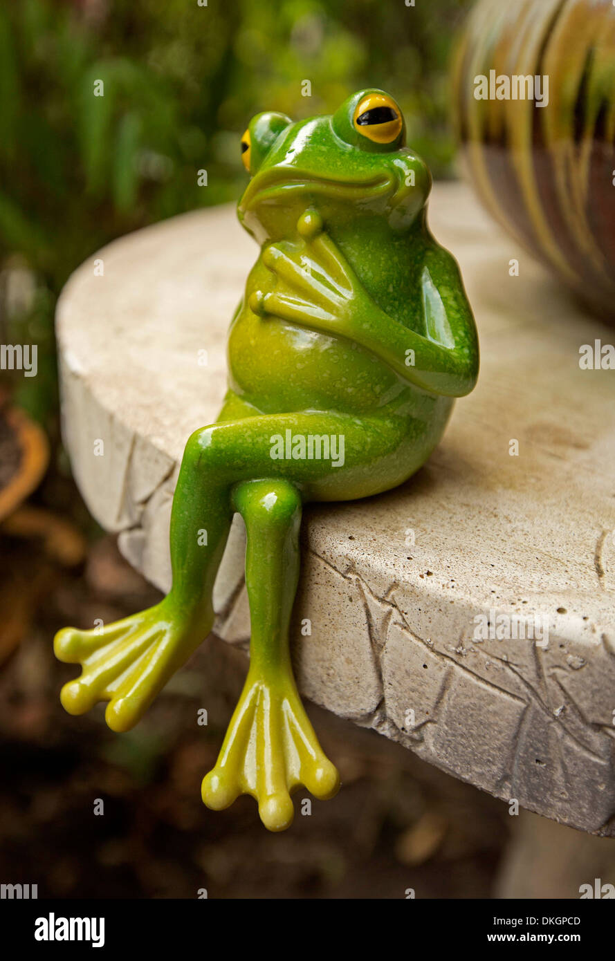 Bright green frog in contemplative pose - garden ornament sitting on edge of decorative concrete table in outdoor setting Stock Photo