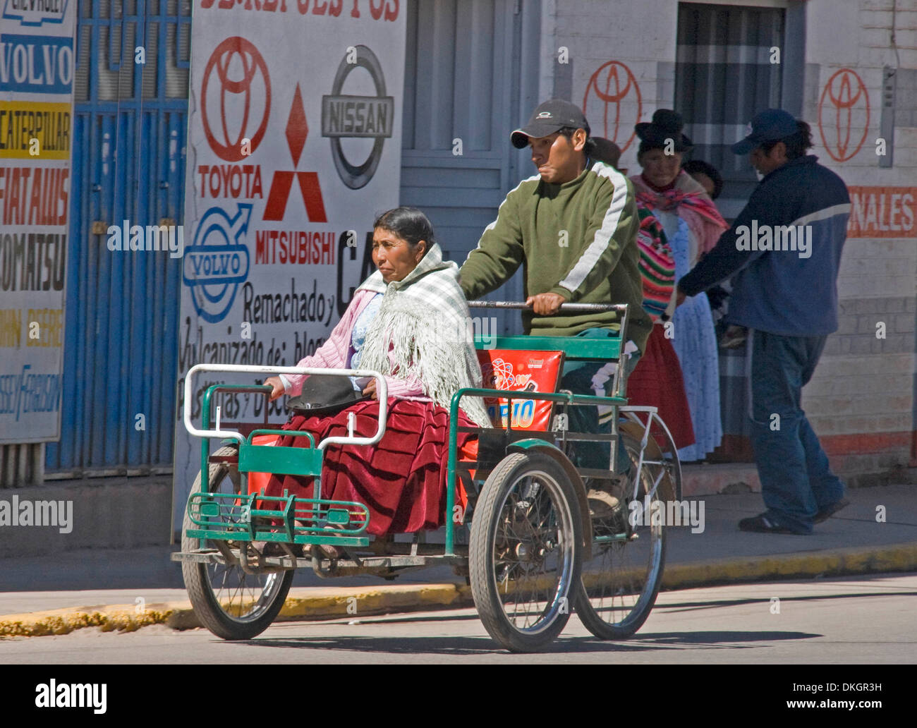 Indigenous woman in traditional dress riding in bicycle taxi with man pedalling along city street in
