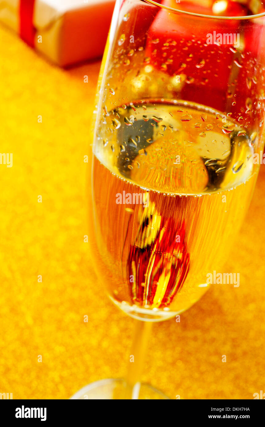 a glass with champagne and some gifts on a golden background Stock Photo