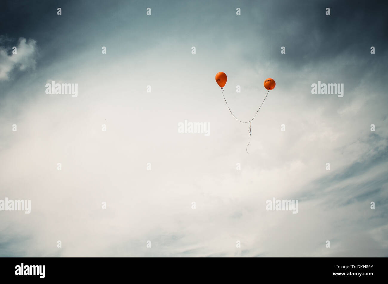 Two orange balloons floating against a cloudy sky Stock Photo