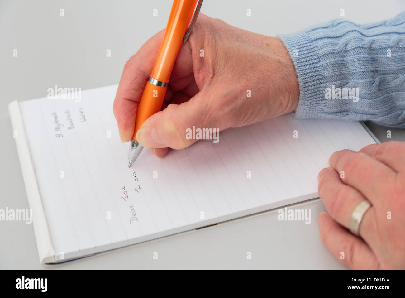 Top down of a right-handed senior woman's hand holding a pen writing a letter on a notepad of paper on a tabletop. England UK Stock Photo