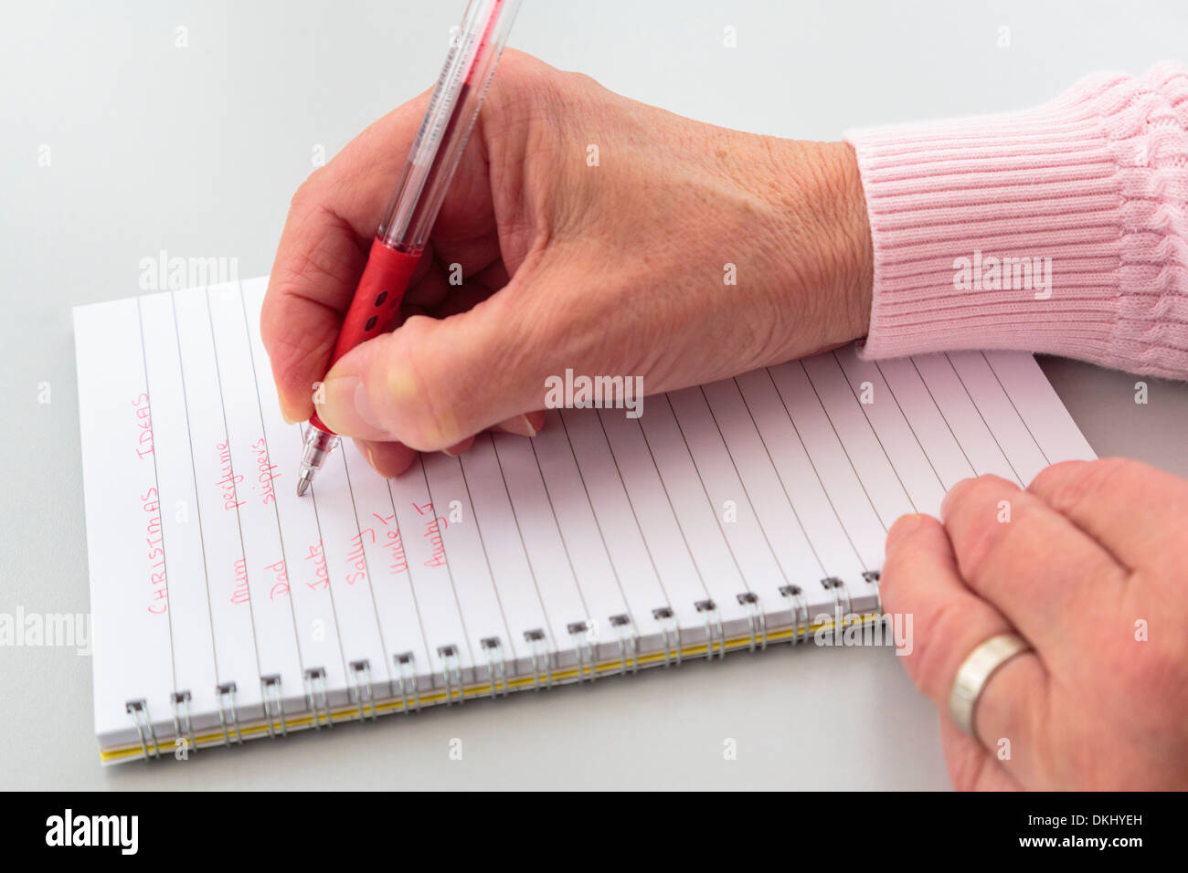 A right-handed mature woman writing a Christmas list of ideas for presents in a notebook on a tabletop. England UK Stock Photo