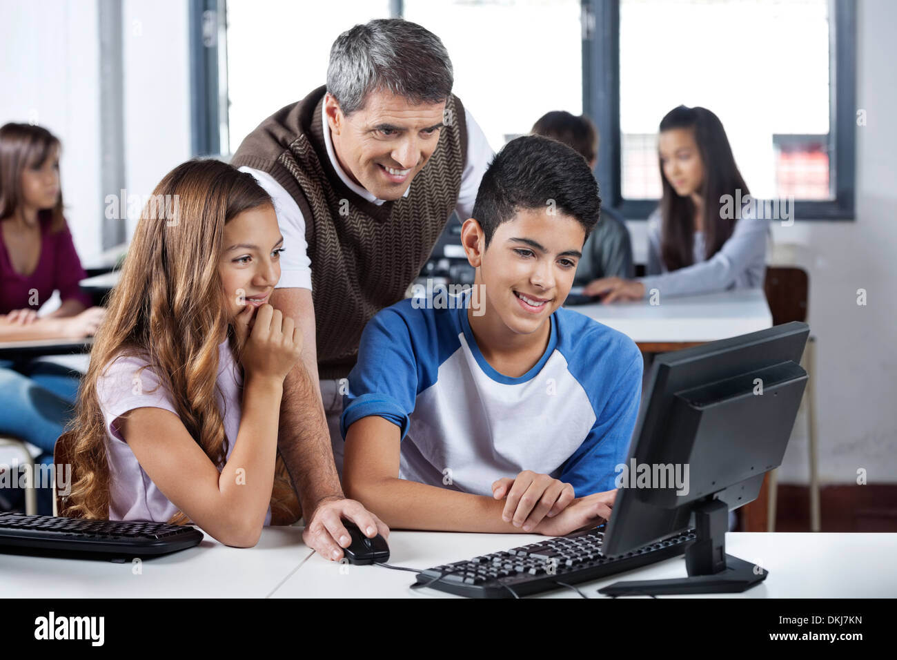 Happy Mature Teacher And Students Using Computer Stock Photo