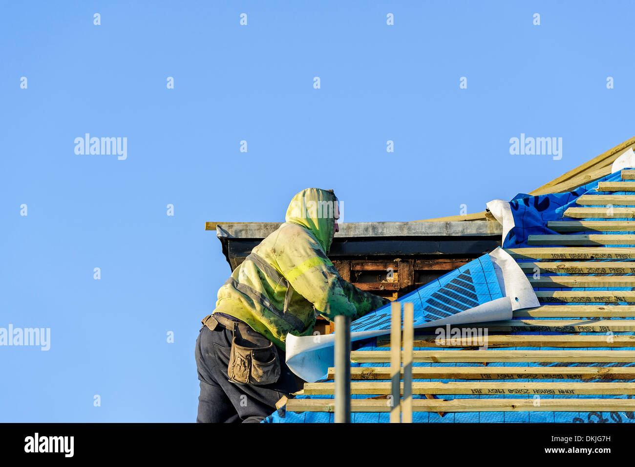 A roofer working near a dormer window whilst replacing a cedar shingle roof on a sunny day. Home improvement project concept Stock Photo