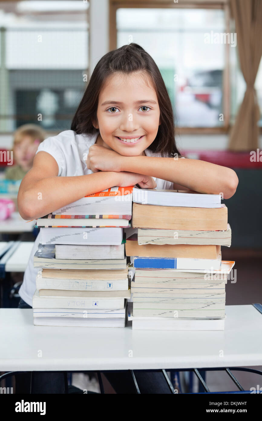 Schoolgirl Leaning On Stacked Books At Desk Stock Photo - Alamy