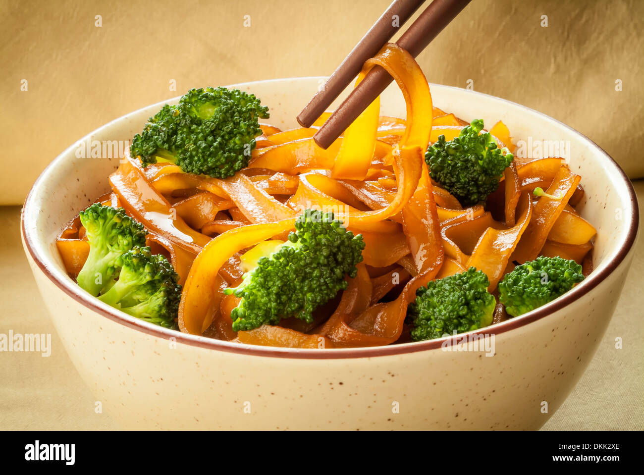 An closeup image of a bowl of broad rice noodles prepared with soy sauce and broccoli with chopsticks. Stock Photo