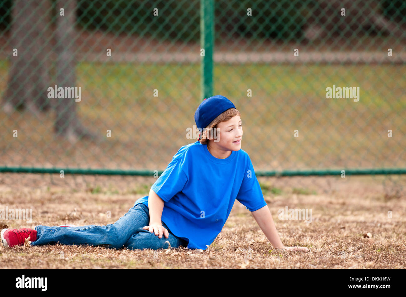 Cute boy playing backyard baseball sitting on grass Stock Photo