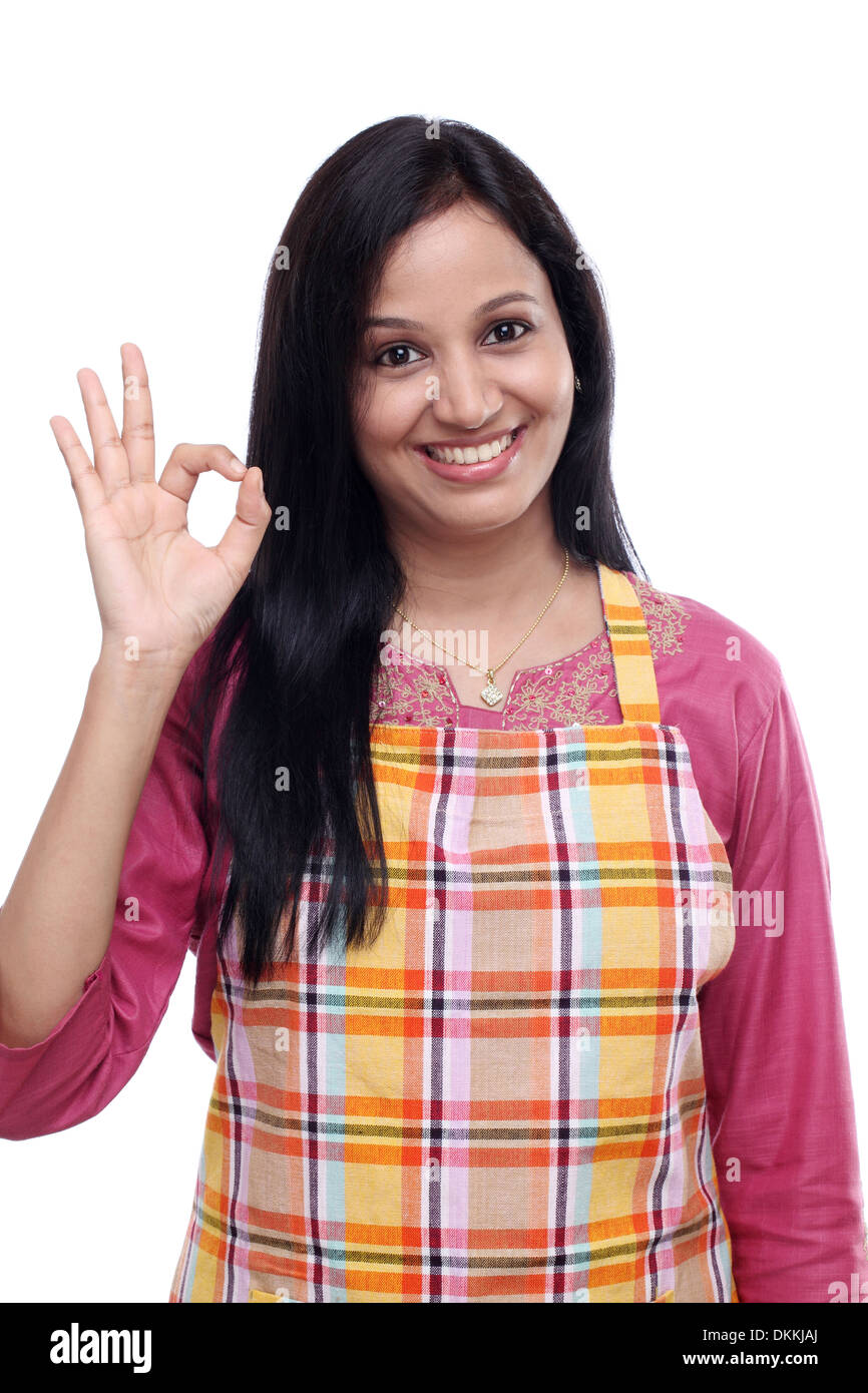 Happy young Indian woman wearing kitchen apron and showing ok sign Stock Photo