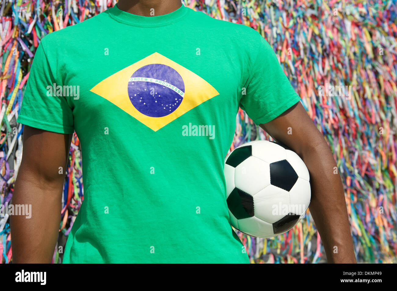 Brazilian soccer player stands with football in front of wall of colorful lembranca wish ribbons in Salvador Brazil Stock Photo