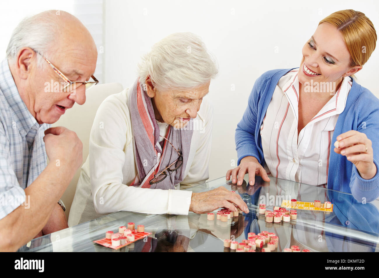 Senior couple playing Bingo with eldercare assistant in nursing home Stock Photo