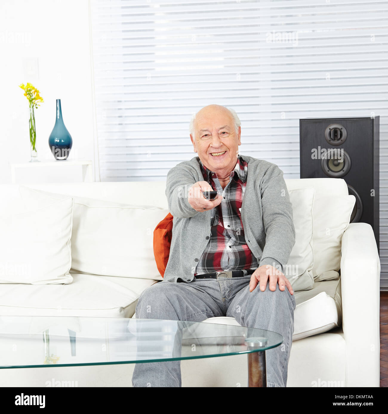 Happy old man with remote control watching TV at home Stock Photo