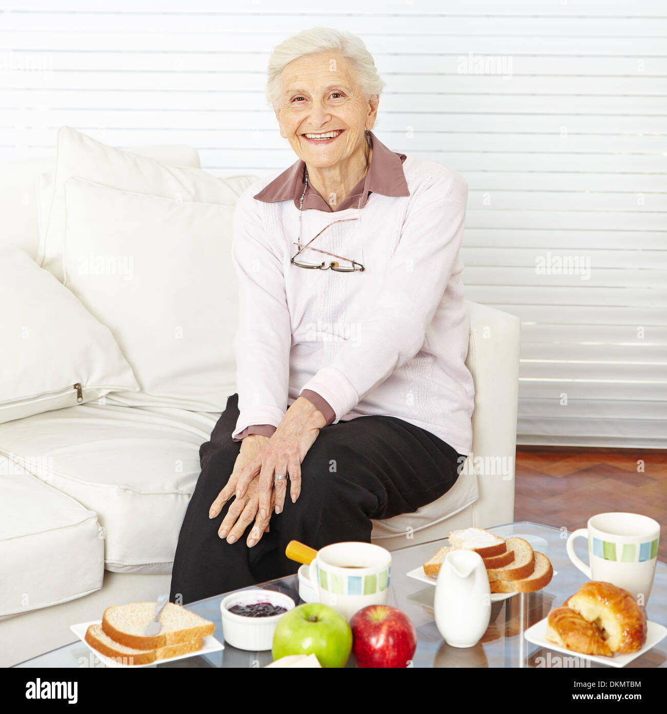 Old smiling woman sitting at set breakfast table at home Stock Photo