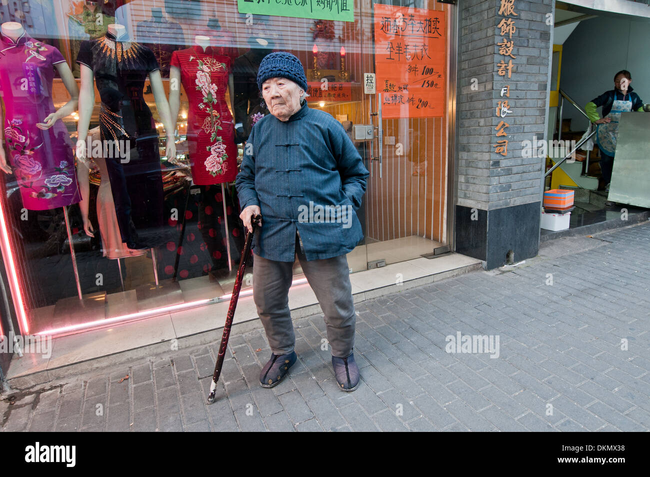 Old Chinese woman in front of clothes shop in Shanghai, China Stock Photo