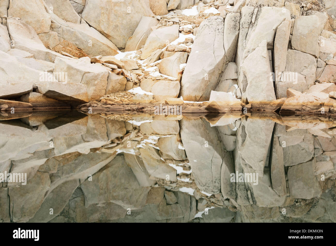 reflection of granite rocks and snow in a still mountain lake Stock Photo