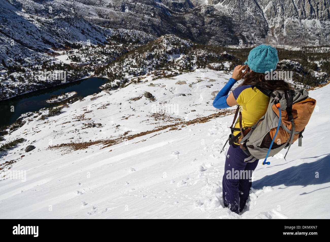 a woman hiking in the snow looks down on a distant herd of deer Stock Photo