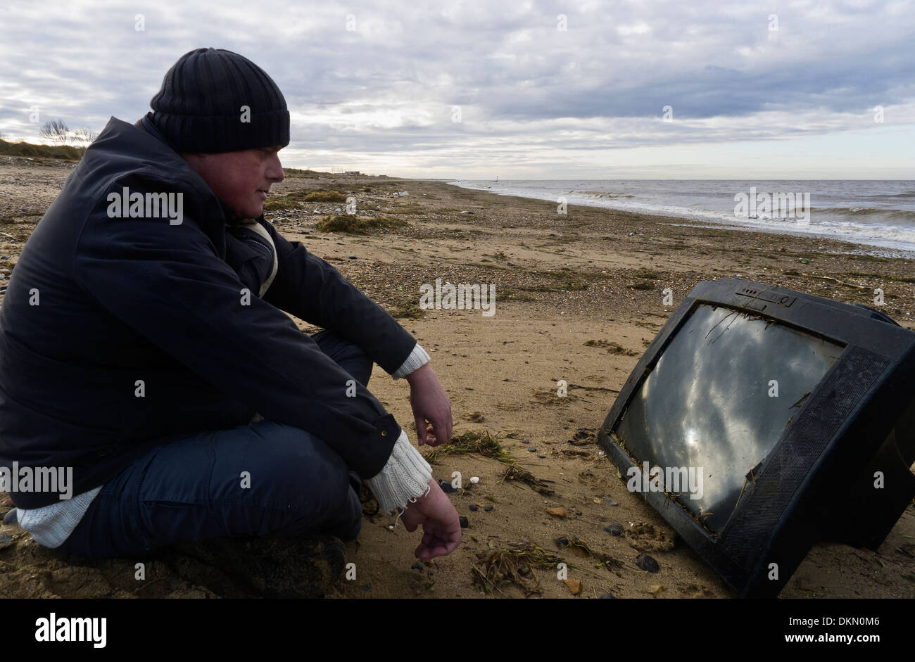 Man watching a television set washed up on a beach. Stock Photo