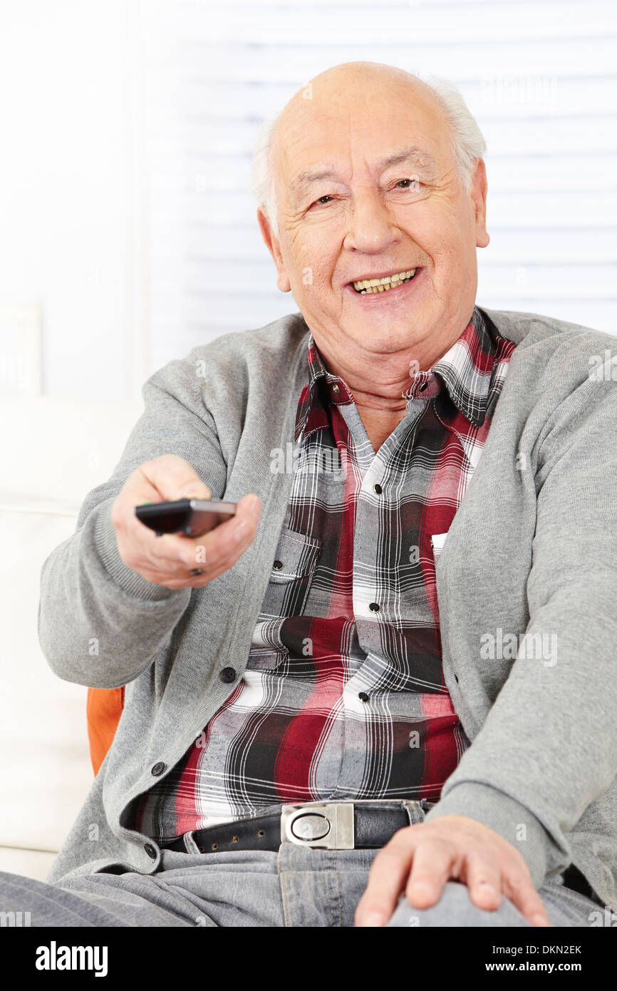 Senior citizen man with remote control watching TV at home Stock Photo