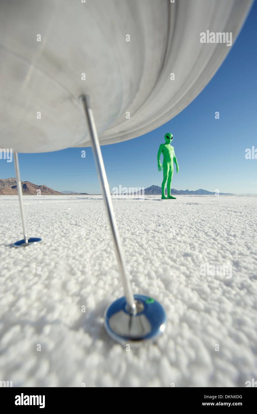 Little green man alien viistori standing under his flying saucer spacehip on strange planet surface Stock Photo