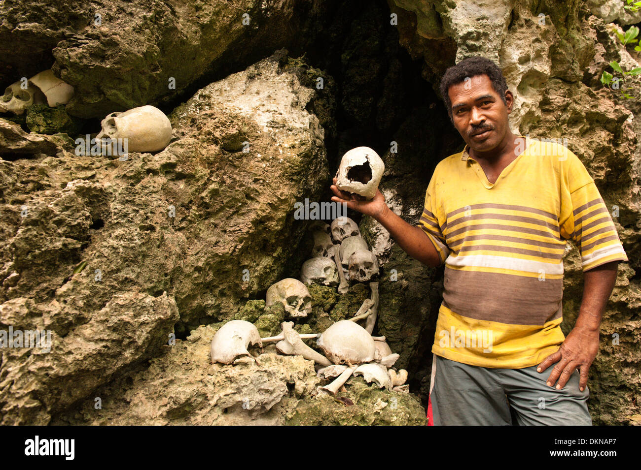 Man holding skull amongst human remains he said were from enemies killed and eaten by his ancestors, renowned warriors. Fiji Stock Photo