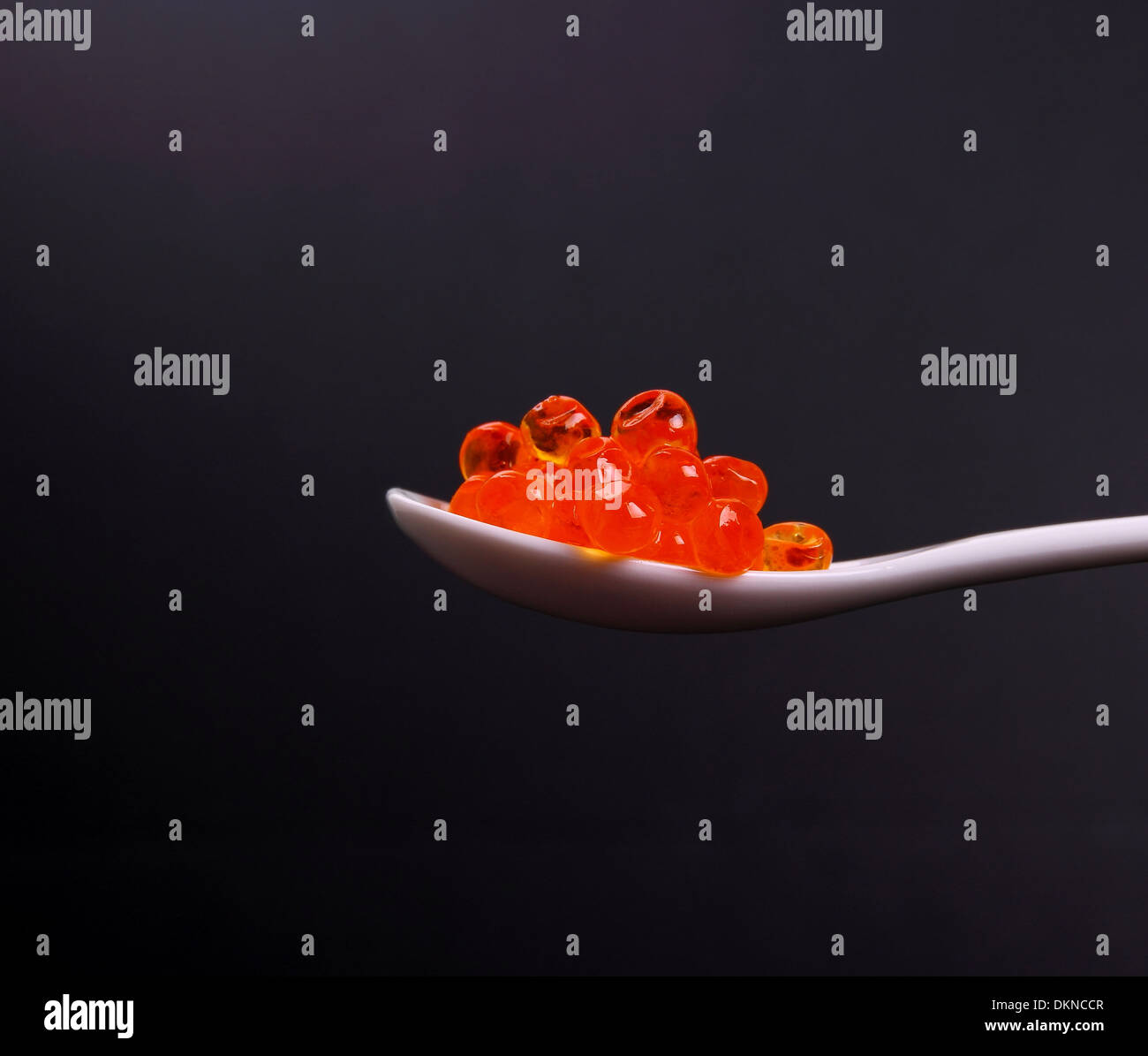 Porcelain spoon full of red caviar on black background, close up Stock Photo