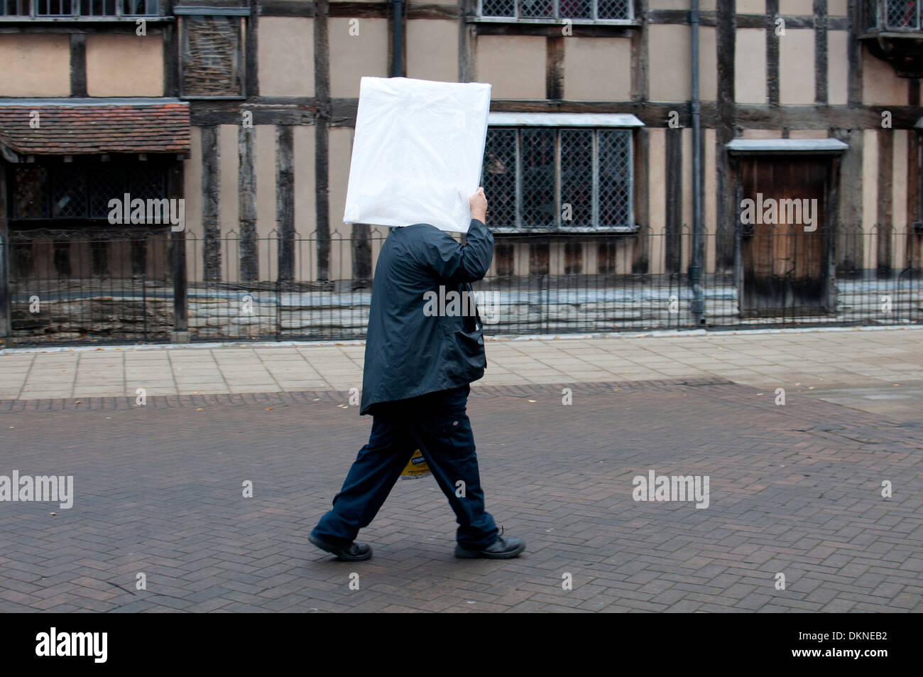 Man carrying a wrapped picture on his shoulder, obscuring his head. Stock Photo