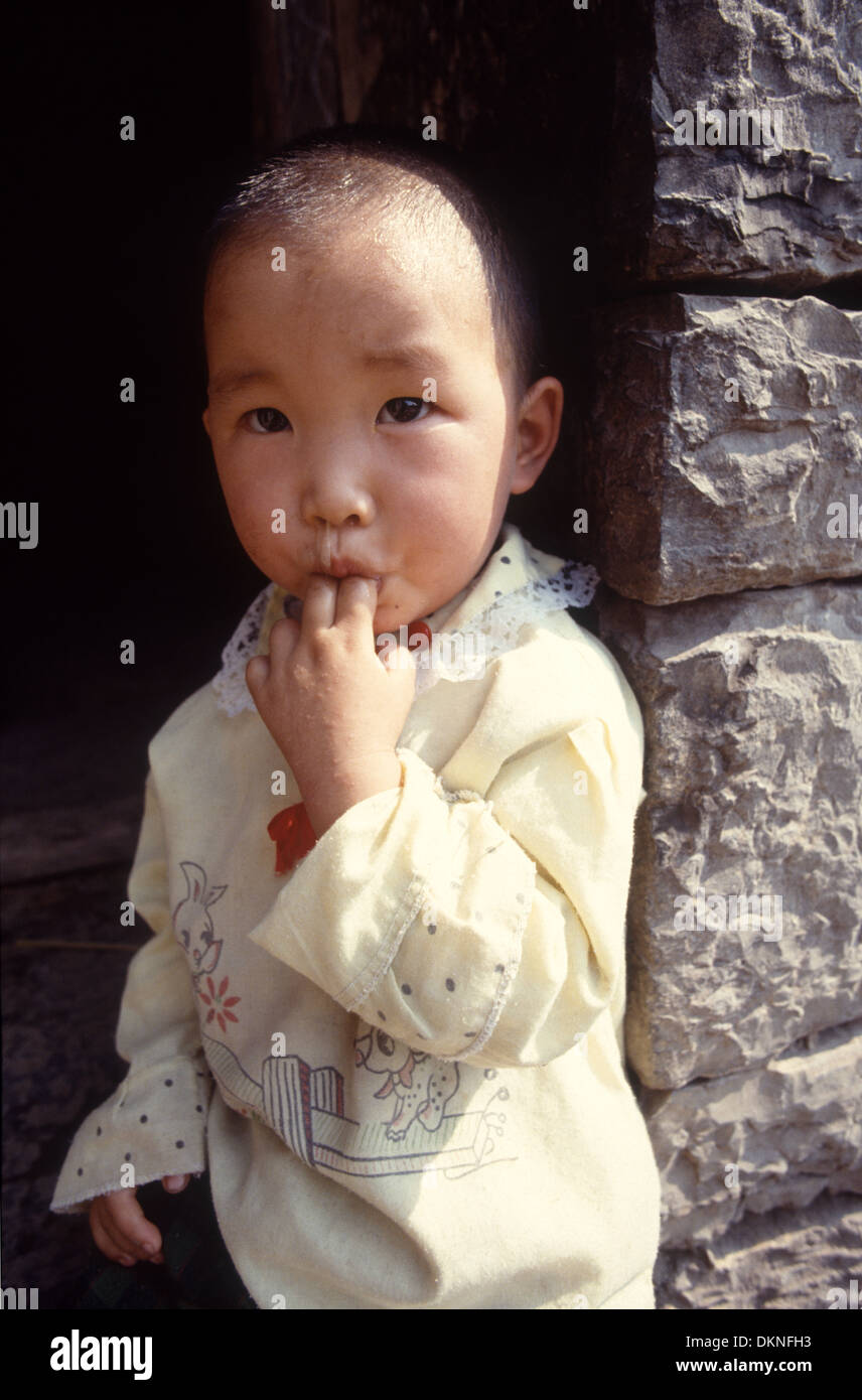 A small girl is sucking fingers, sitting outside the front door of her primary school in Hunan Province, China Stock Photo
