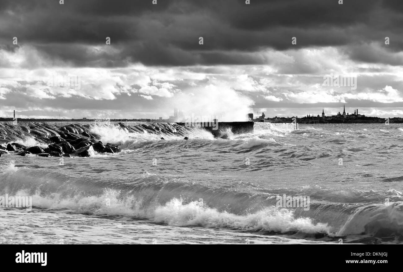 Pier or quay in a stormy and turbulent sea at a gloomy but but sunny day. City silhouette of Tallinn in background. Stock Photo