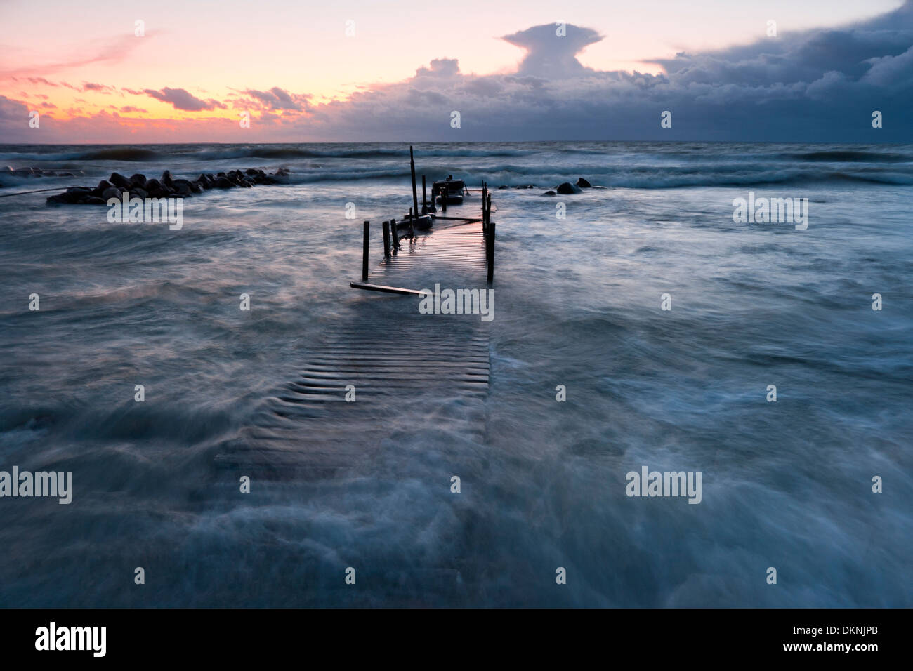 Timber foot bridge in sea and partly under water due to high tide at sunset Stock Photo