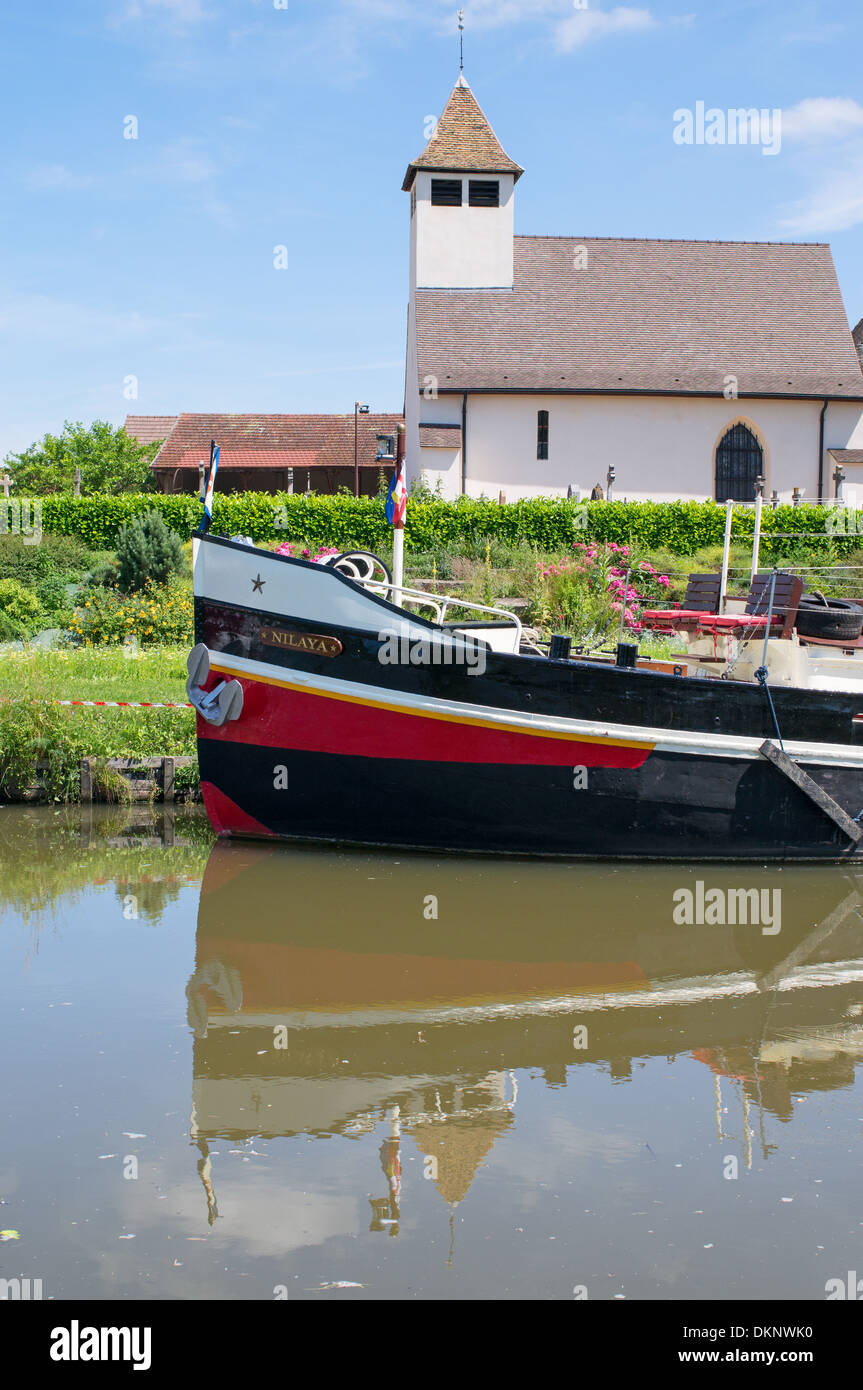 Canal boat Nilaya moored in Canal du Centre before village church Burgundy eastern France Stock Photo