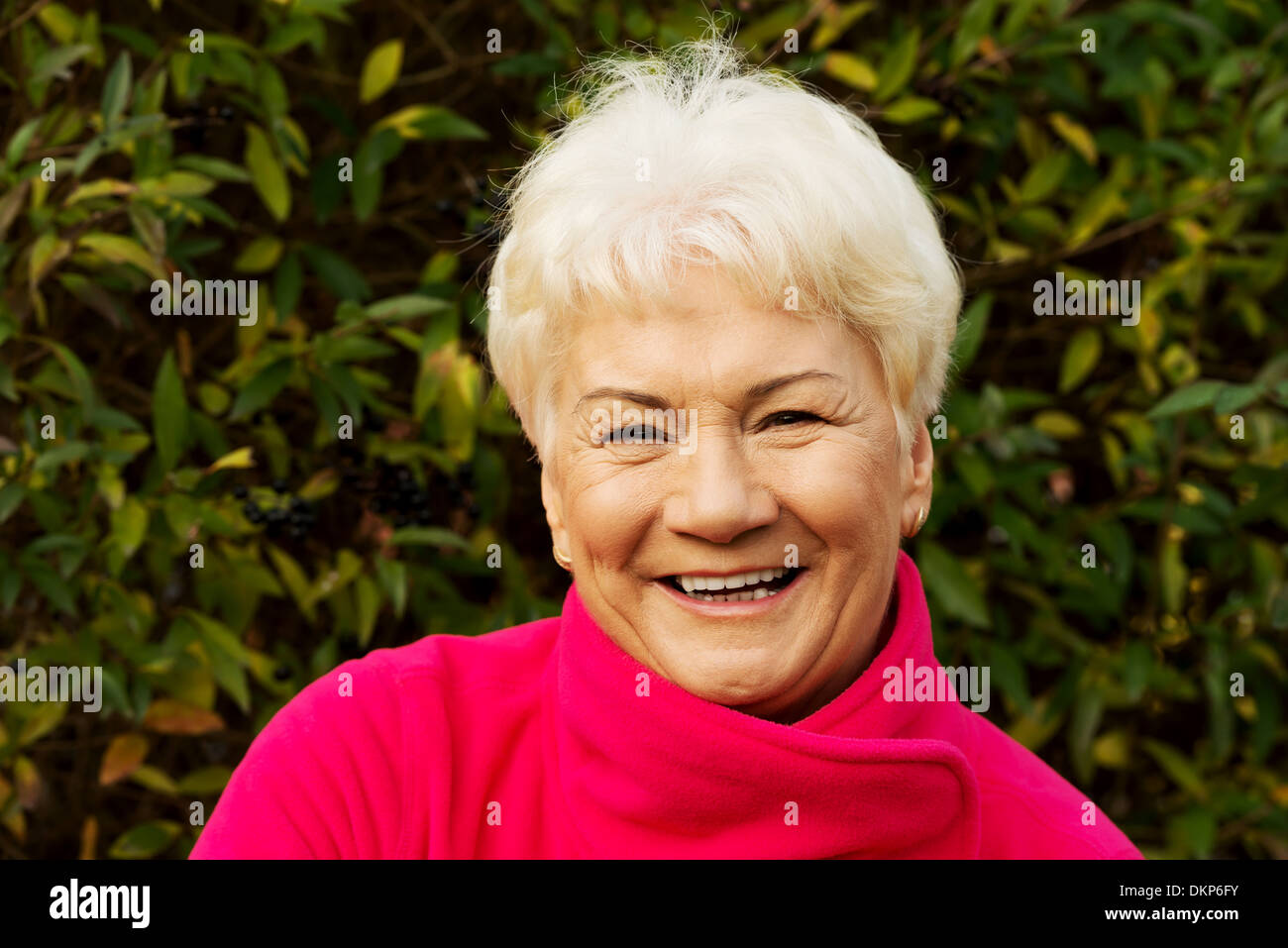 Portrait of a cheerful old lady over green background. Outdoor.  Stock Photo