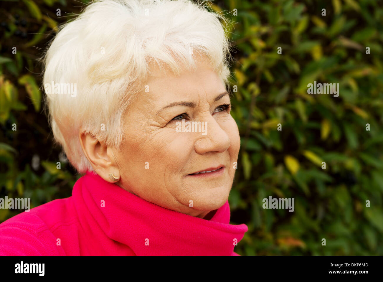 Portrait of a cheerful old lady over green background. Outdoor.  Stock Photo