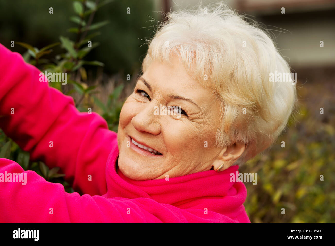 An old lady is cutting bushes. Outdoor background.  Stock Photo