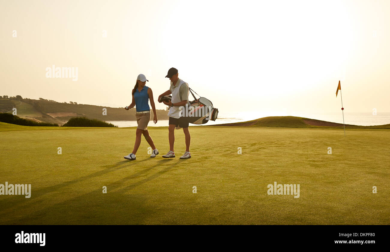 Caddy and woman walking on golf course overlooking ocean Stock Photo