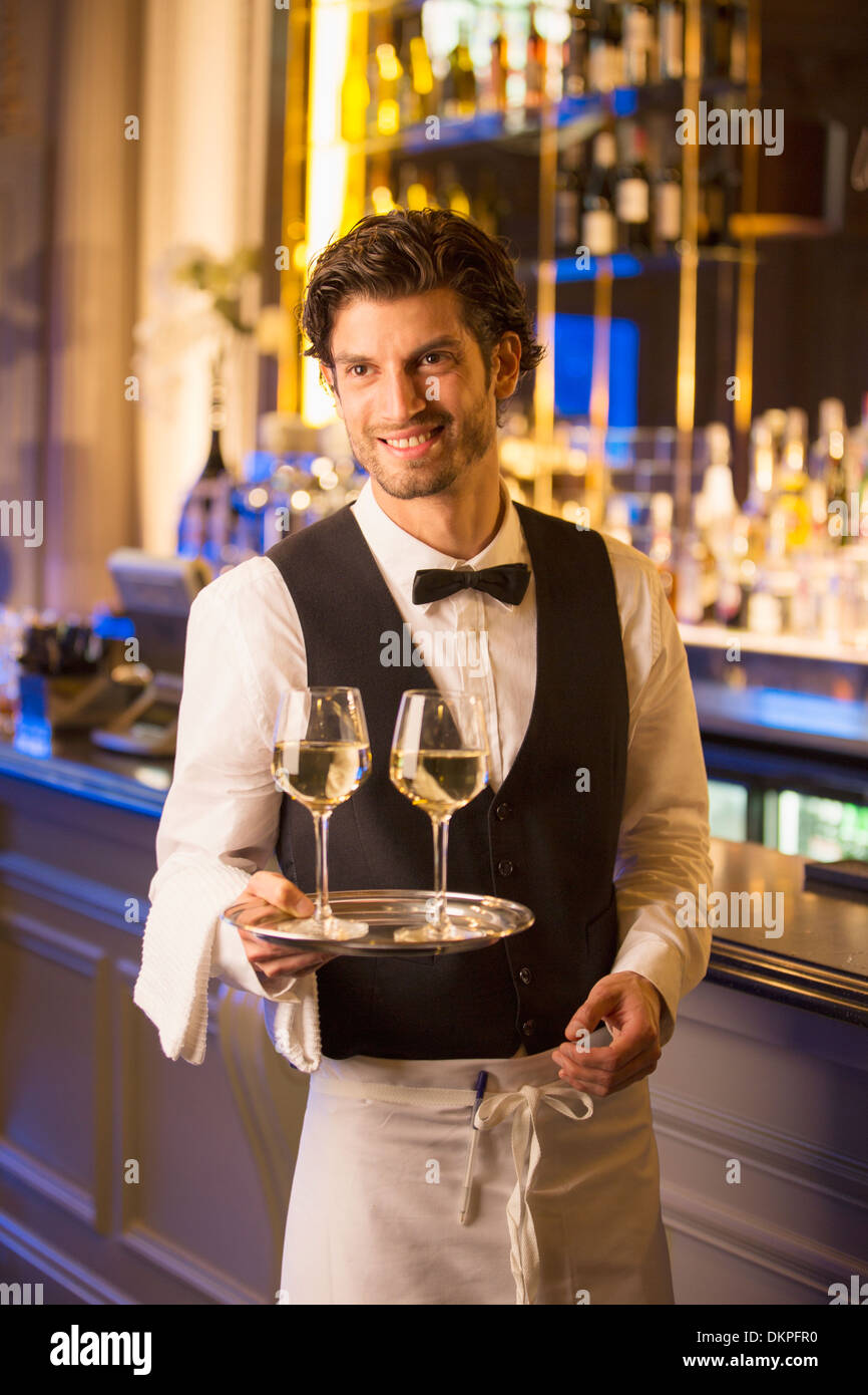 Well dressed bartender carrying wine glasses on tray in luxury bar Stock Photo