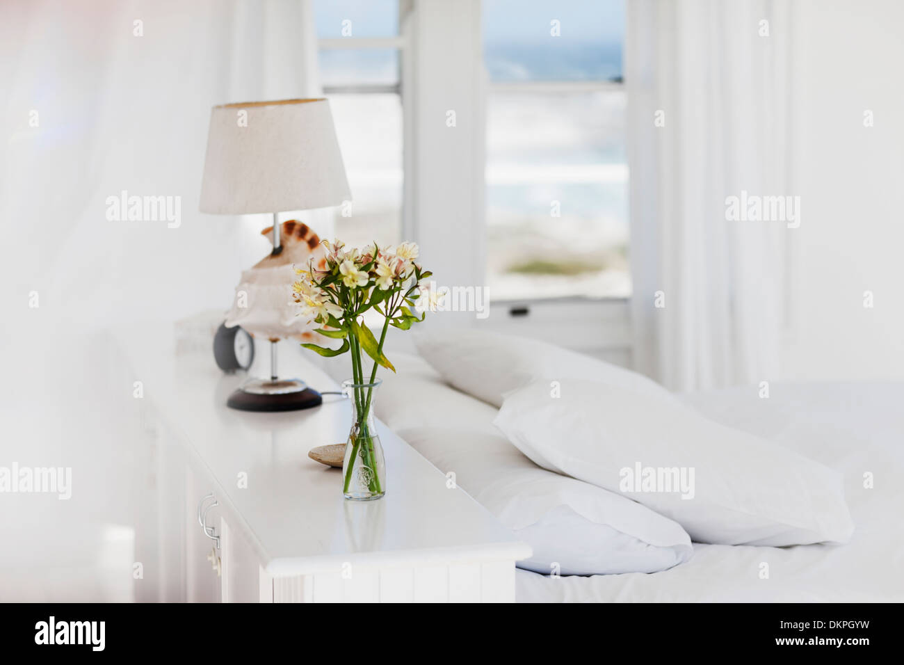 Vase of flowers and lamp in white bedroom Stock Photo