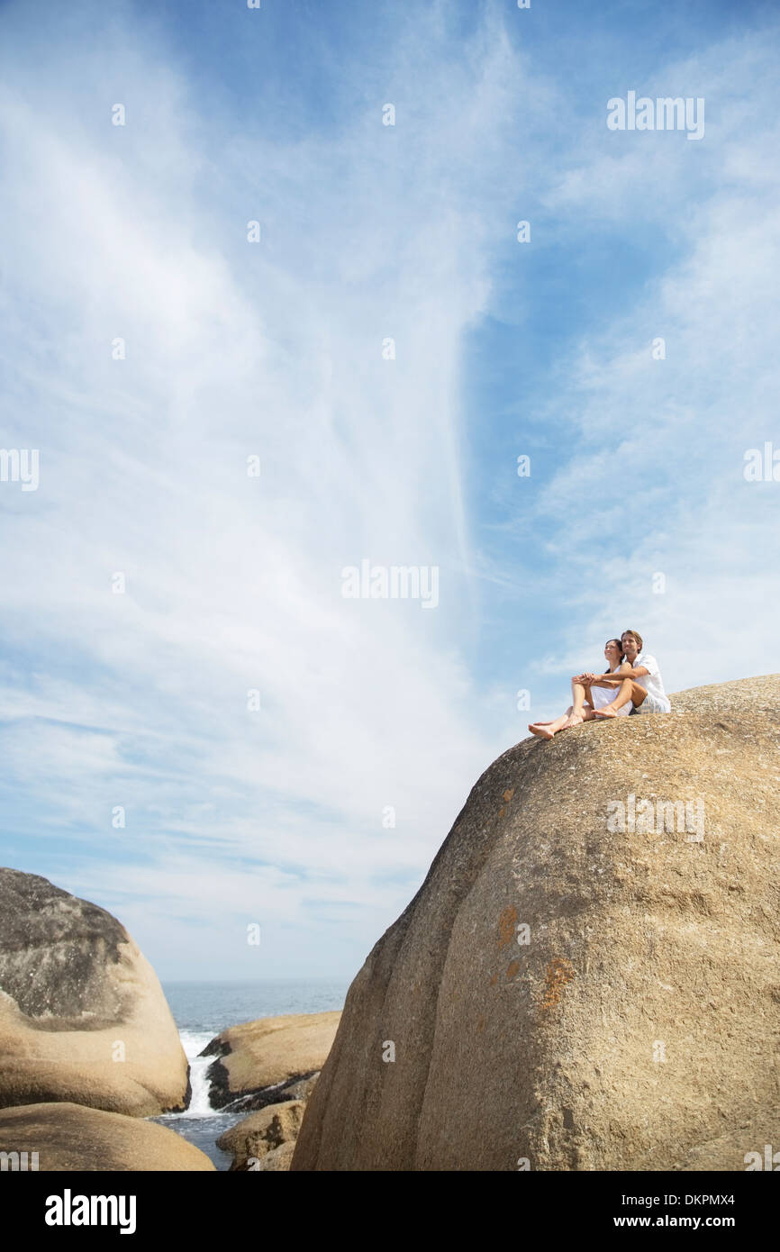 Couple sitting on rock formation on beach Stock Photo