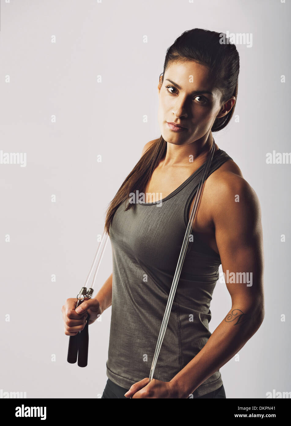 Confident young mixed raced female athlete posing with jumping rope looking at camera. Muscular woman with skipping rope Stock Photo