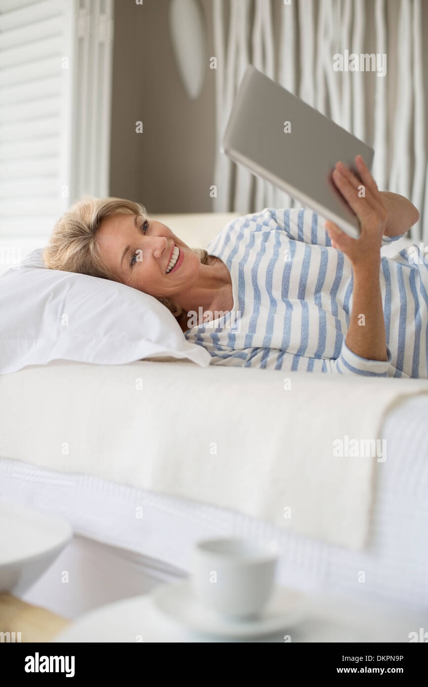 Older woman using digital tablet on bed Stock Photo