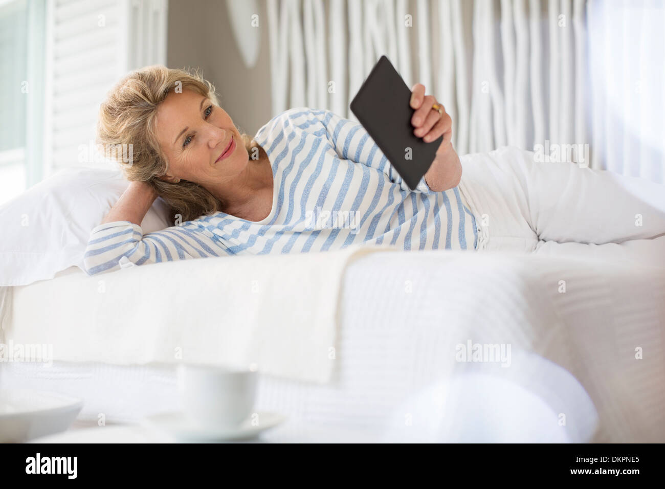 Older woman using digital tablet on bed Stock Photo