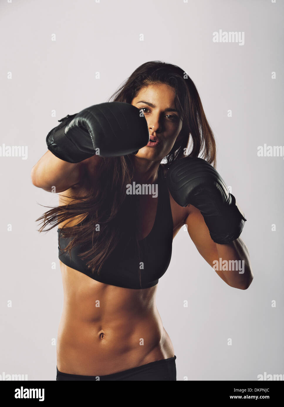 Portrait of young sports woman wearing boxing gloves training boxing. Mixed race female practicing boxing looking at camera. Stock Photo