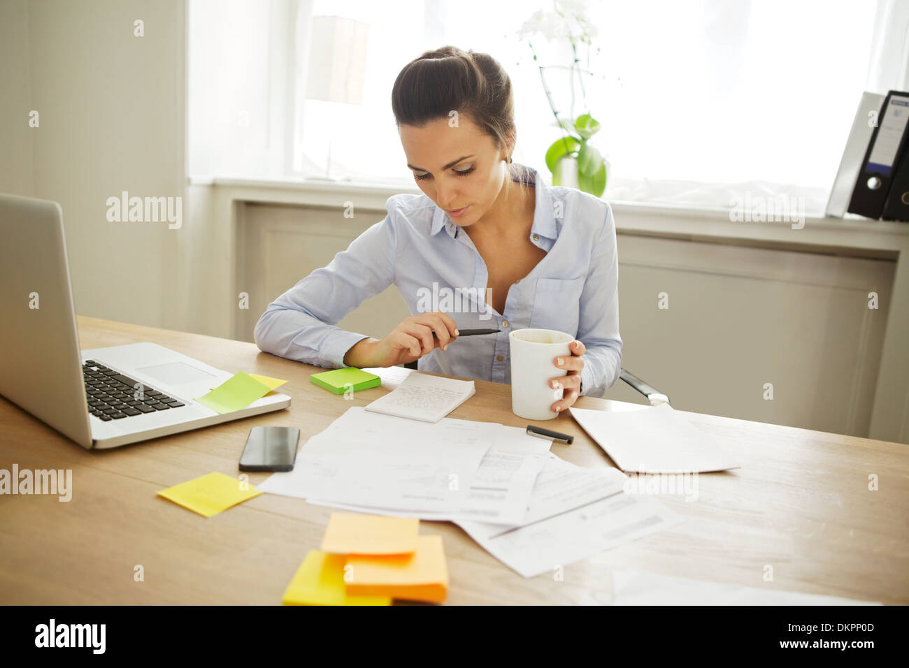 Attractive young woman working at the desk with sticky notes and laptop. Beautiful businesswoman reading notes while sitting Stock Photo