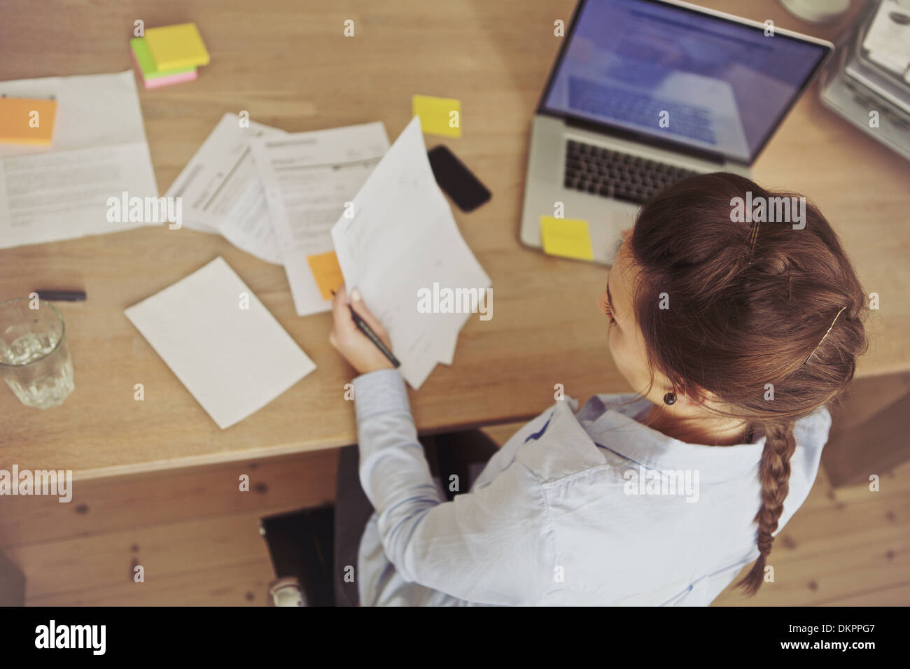 Top view of young woman checking bills while sitting at the desk with laptop. Caucasian businesswoman working at the desk. Stock Photo