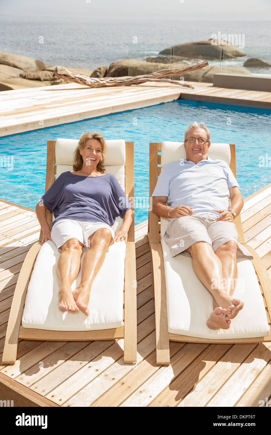 Senior couple laying on lounge chairs at poolside Stock Photo