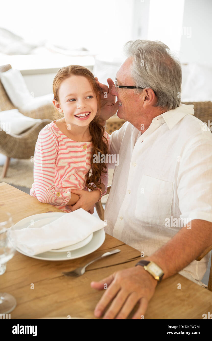 Older man and granddaughter whispering at table Stock Photo
